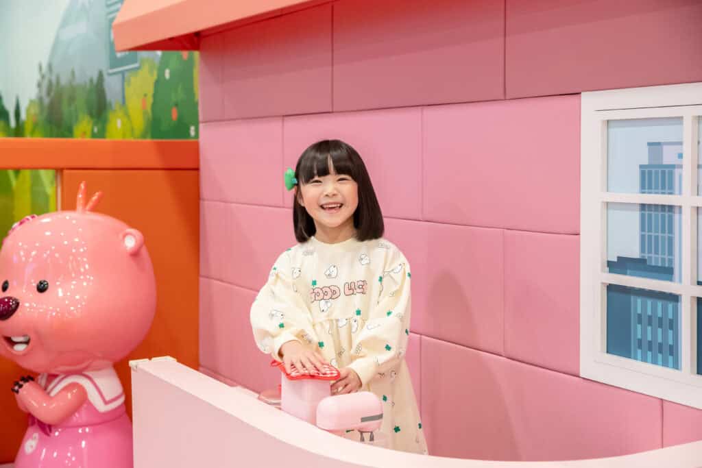 뽀로로파크 금천점 루피의 마트놀이 존 키즈모델 체험 이미지 행주로 기물 닦고 있으며 활짝 미소짓는 모습